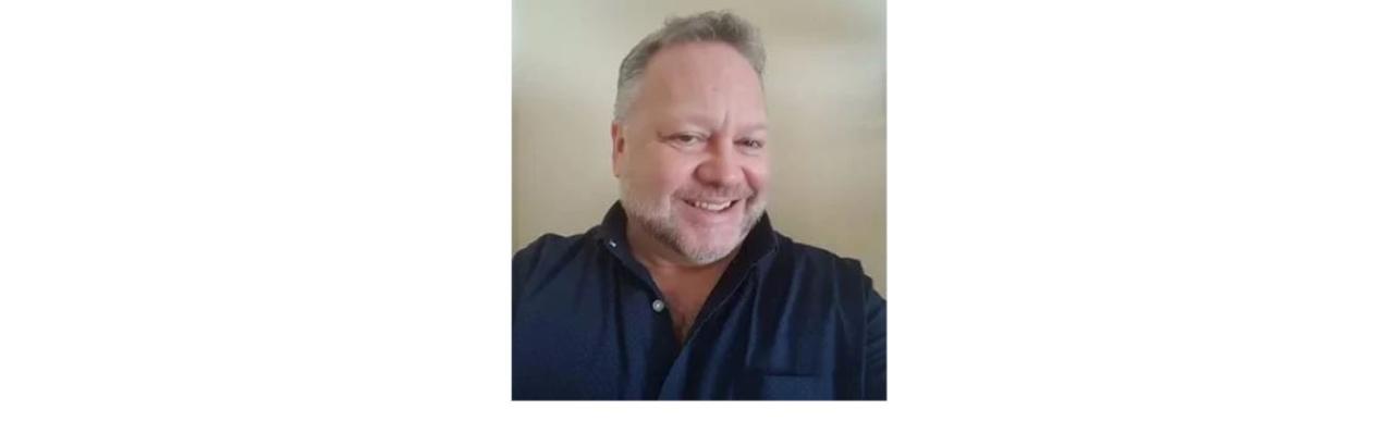 color photo of Bob Sattler, a middle aged white mad with a grey beard and grey hair wearing a black button down shirt