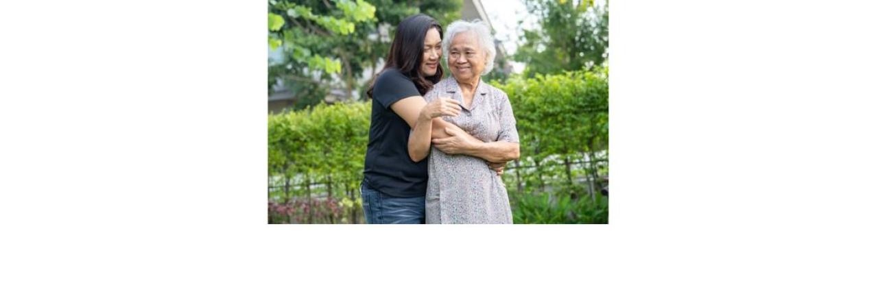color photo of a young Asian woman in jeans and a black t shirt hugging an older Asian woman in a lavender dress