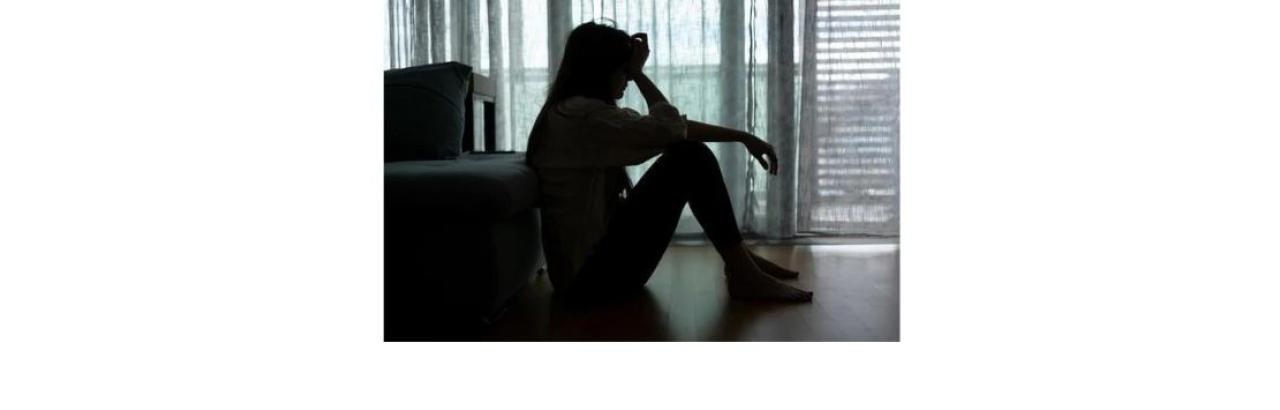 a silhouette of a young woman sitting on the floor with her head in her hands 