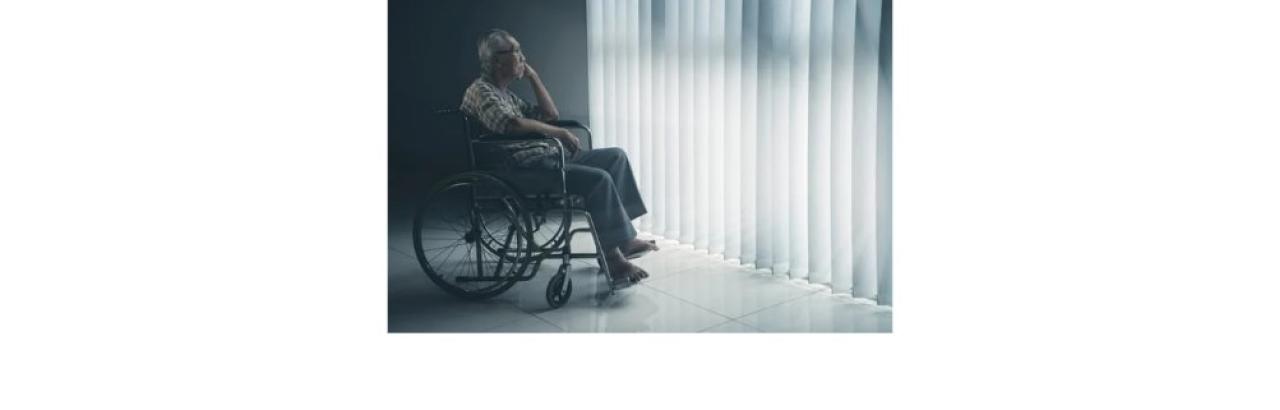 photo of an older Asian man with grey hair and glasses sitting in a wheelchair looking out a window