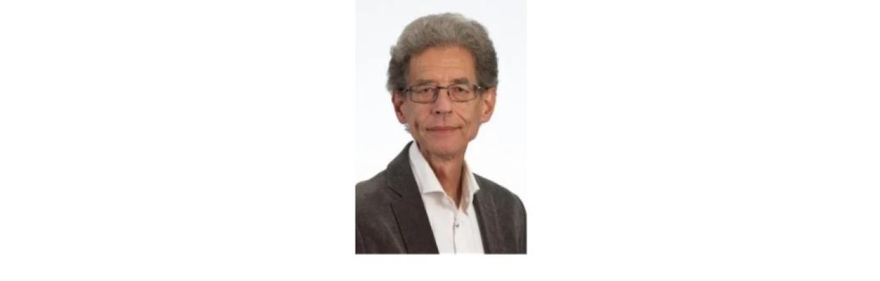 Color photo of Marcel Post, an older white man with grey curly hair and glasses wearing a black cardigan over a white shirt