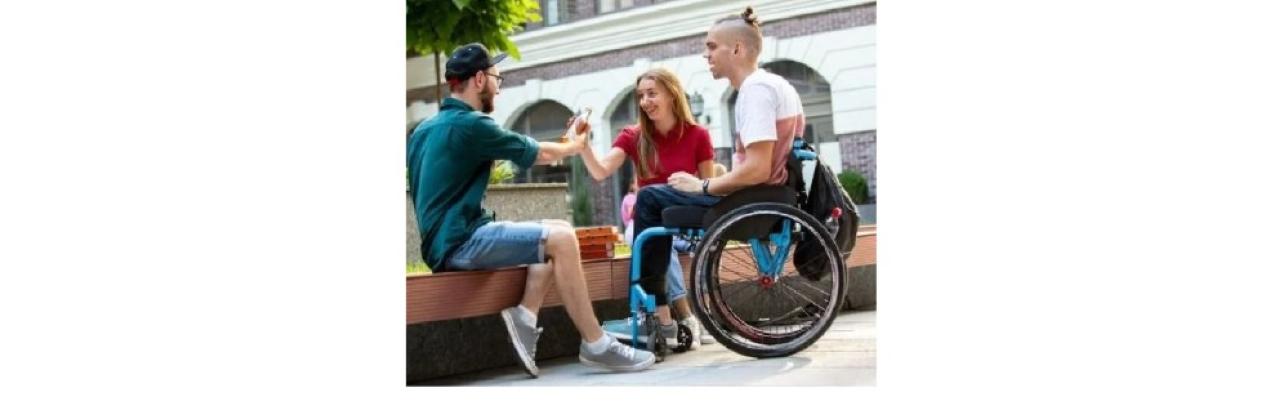photo of three young adults sitting together outside. One young man is in a wheelchair