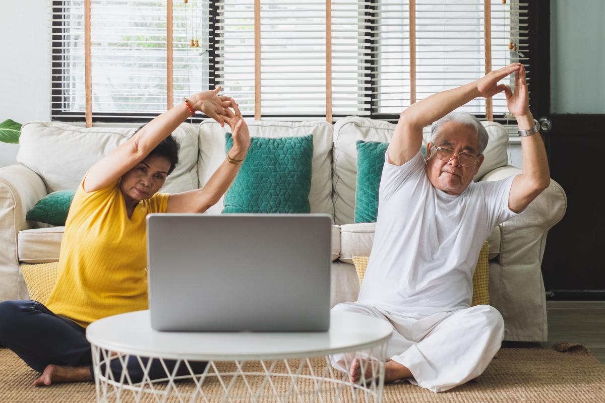 Man and woman do seated yoga at home using laptop