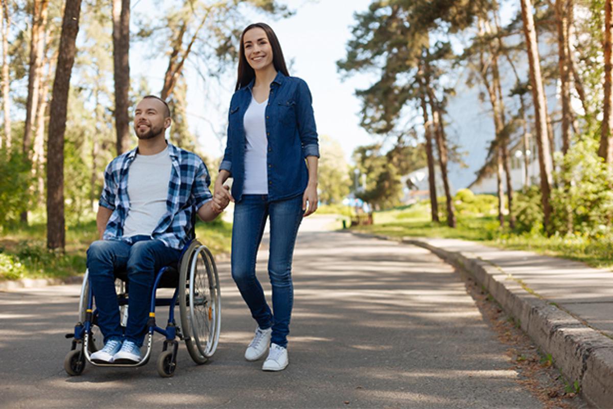 A man using a wheelchair and a woman hold hands outside.