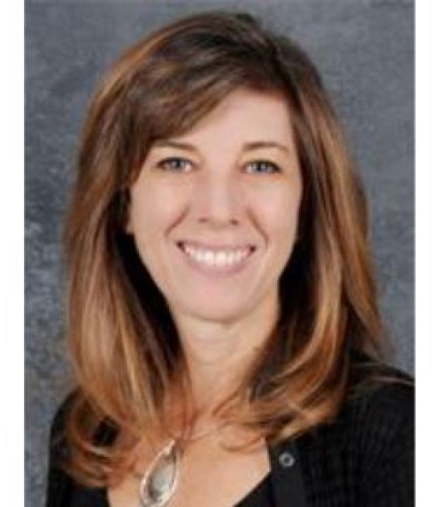 white woman with shoulder length brown hair and a black shirt smiling.