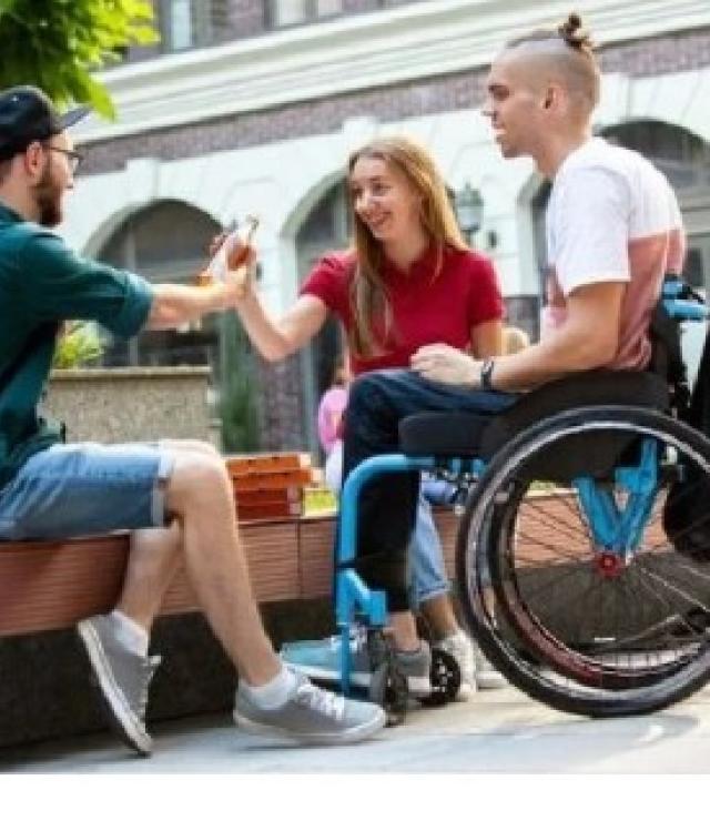 photo of three young adults sitting together outside. One young man is in a wheelchair