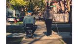 A person in a wheelchair with caregiver walking on a sidewalk