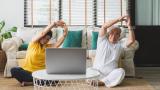 Man and woman do seated yoga at home using laptop