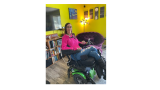 This image shows Maggie Winston in her wheelchair wearing a pink sweater and jeans. 