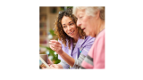 A direct care worker is supporting an elderly woman in reading a magazine.