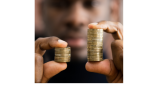 A black man is holding two stacks of gold coins in each hand. The stack of coins in the left hand is smaller than the stack of coins in the right hand.