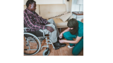 black man in wheelchair with woman in nurse clothing and headscarf adjusts his foot rest