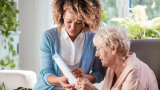 a white woman who is a senior citizen and a young black woman are reading a document together