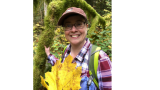 Woman with glasses smiling and holding a large leaf. She is outdoors