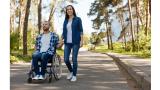 A man using a wheelchair and a woman hold hands outside.