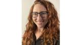 Young white woman with long red curly hair and black rimmed glasses is smiling.