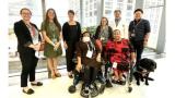 group photo of 8 people, two in wheelchairs one black service dog