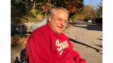 Middle aged man with grey hair wearing a read sweatshirt sitting in a wheelchair outside in Autumn
