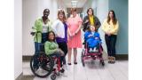 A group of people standing together in a hallway, two are in wheelchairs