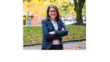 A photo of Carli Friedman, a young white woman with shoulder length brown hair and glasses standing outside