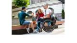 Two young white men and one white woman are sitting outside - one of the men is in a wheelchair.