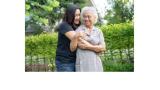 color photo of a young Asian woman in jeans and a black t shirt hugging an older Asian woman in a lavender dress