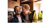 a young man with an intellectual disability is smiling while another young man with red hair holds his shoulders and smiles.