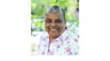 color photograph of Cindy Bently - a middle aged Black woman with short grey hair wearing a white top. She is outside and is smiling