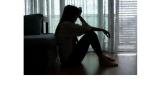 a silhouette of a young woman sitting on the floor with her head in her hands 